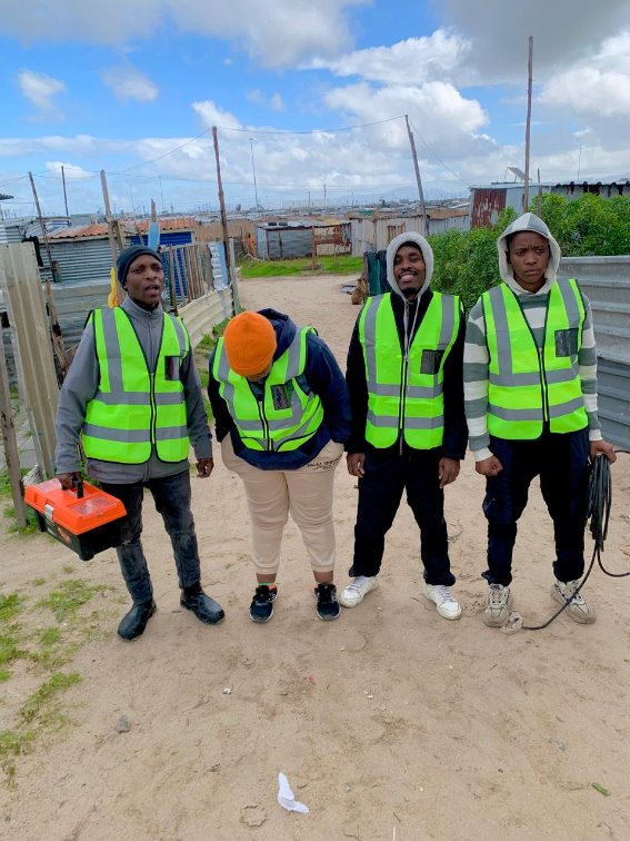 Four Zonke field-team members in high-visibility vests, standing together in a Cape Town settlement.