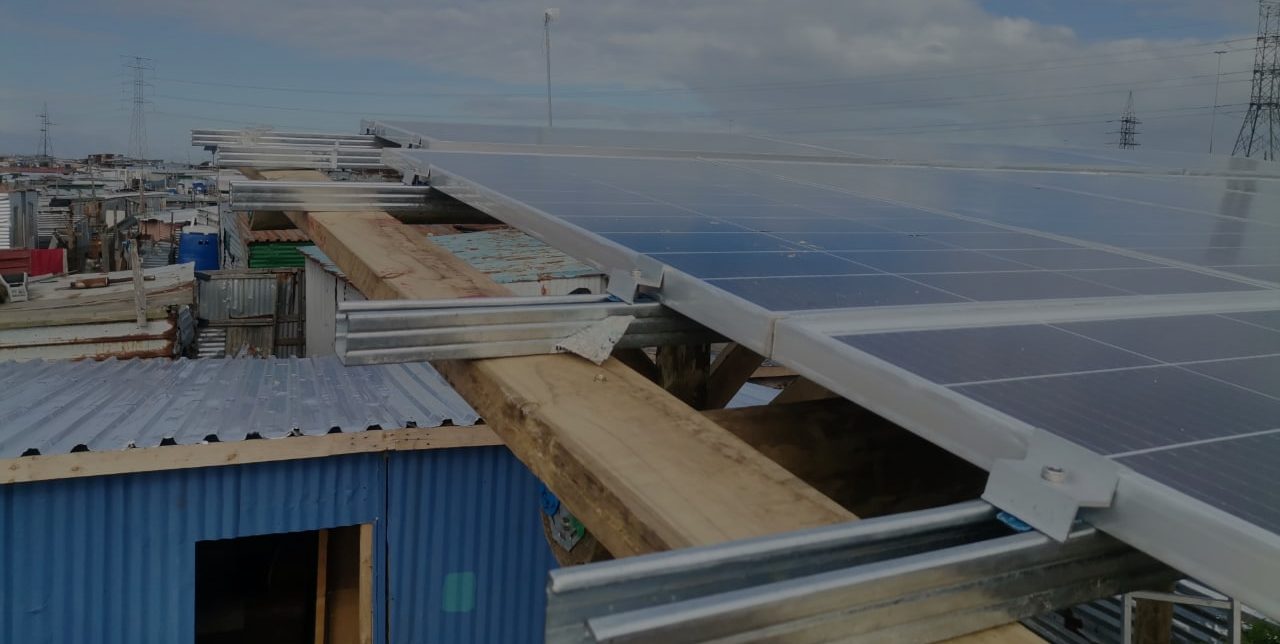 A Zonke solar panel array installed above corrugated-iron shack rooftops in a Cape Town settlement.